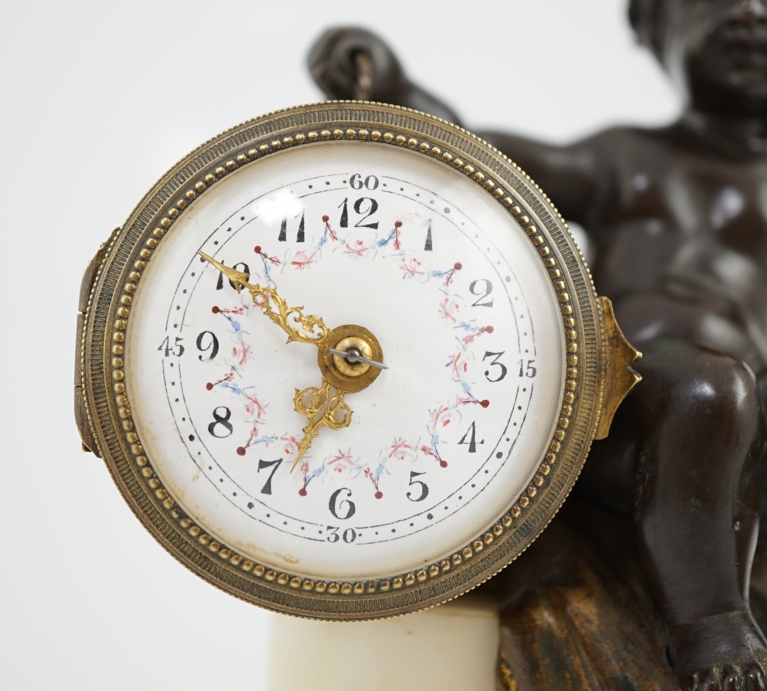 An early 20th century French eight day bronze and ormolu desk timepiece modelled as a putto banging upon a drum, with floral enamelled dial and white marble plinth, 12cm wide, 22.5cm high. Condition - good